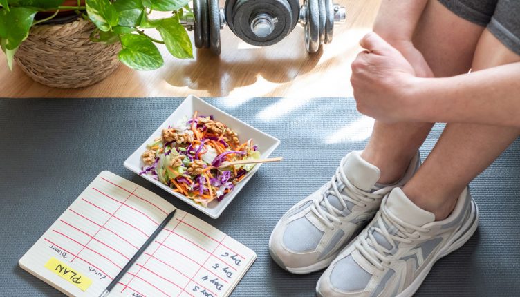 person-tying-a-shoe-next-to-a-meal-plan,-dumbbells-and-a-healthy-bowl
