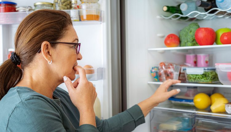 woman-looking-into-an-open-refrigerator-stocked-with-produce