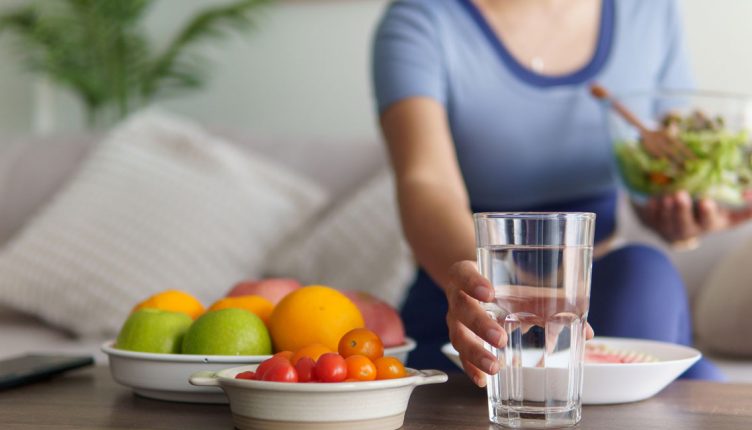 woman-setting-a-glass-of-water-on-a-table-beside-a-bowl-of-fruit